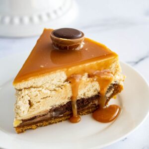 A slice of cheesecake on a white plate. A gold fork sits in front of the plate.