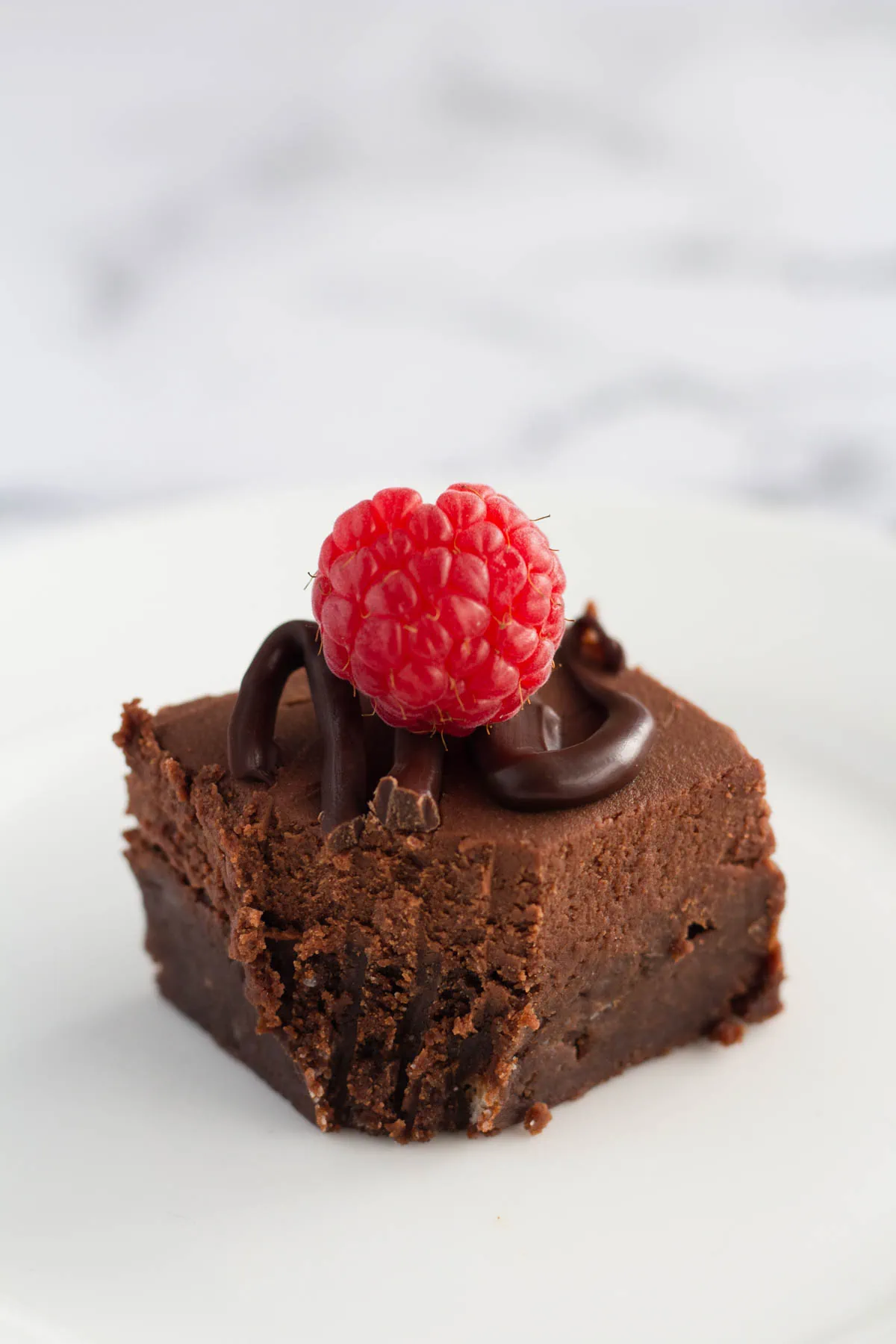 One brownie on a white plate. A fork bite has been taken out of the corner of the brownie.