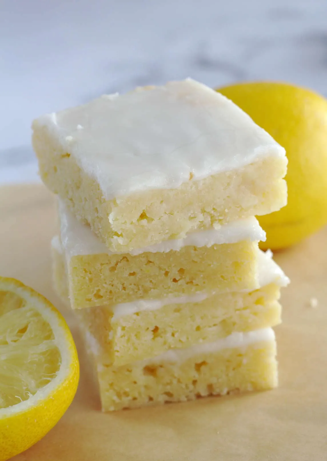 Four lemon brownies stacked on top of each other. Two lemons sit around the brownies.