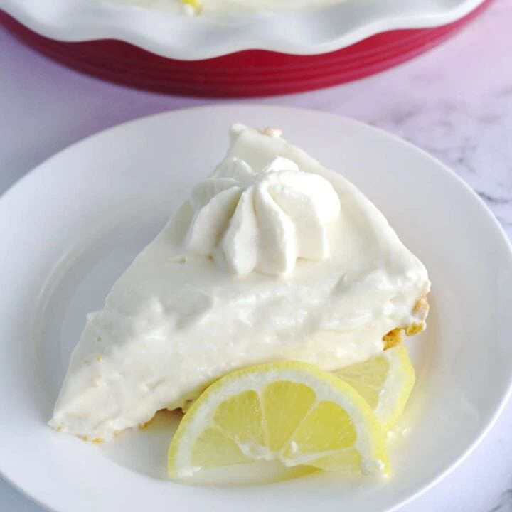 A slice of pie on a white plate. Two slices of lemon are on the plate in front of the pie.