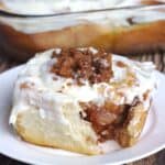 A cinnamon roll on a white plate with a forkful from it. You can see the apple filling inside.