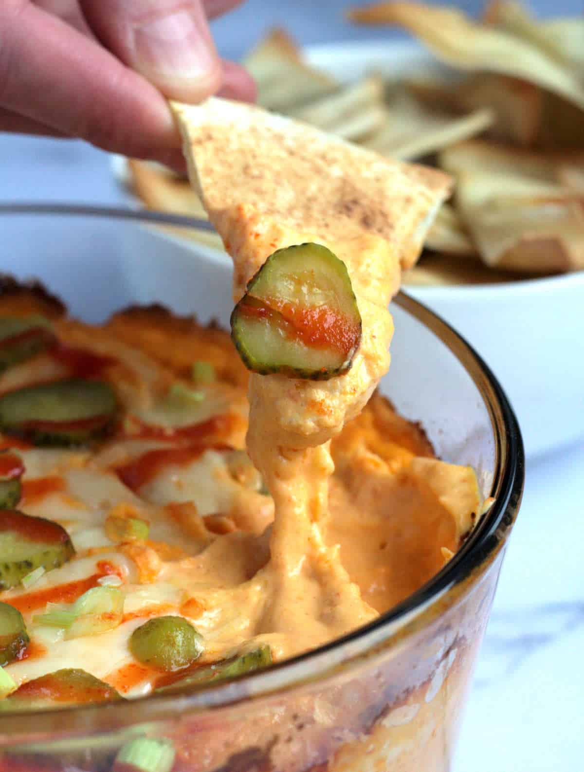 A dip with a person's hand dipping a pita chip into it.