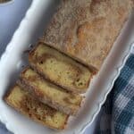 A loaf on a white rectangular serving plate. A few pieces of the loaf is cut , and the pieces are laying in their spots.