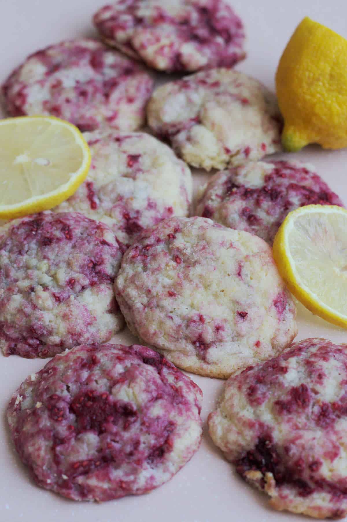 Cookies scattered around on a pink cookie sheet. Several lemon slices are scattered around the cookies.