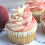 A cupcake with a few more around it. Some peaches are laying around the cupcakes.