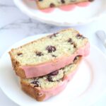Two slices of loaf cake on a white plate. The rest of the loaf cake is in the background on a white cake plate.