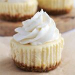 One mini cheesecake on a piece of parchment paper. More mini cheesecakes are in the background.