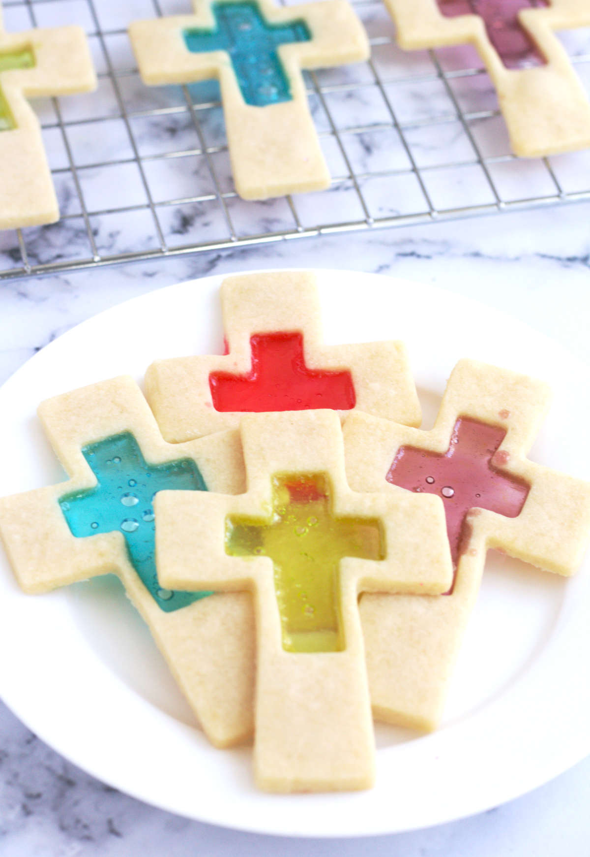Four cookies on a white plate. The rest of the cookies are on a wire rack in the background.