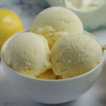 Three scoops of ice cream in a white bowl. A lemon is in the background.