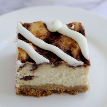A single cinnamon roll cheesecake bar on a white plate.