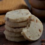 A stack of five cookies with another cookie leaning on the stack of cookies. It has a bite out of it.