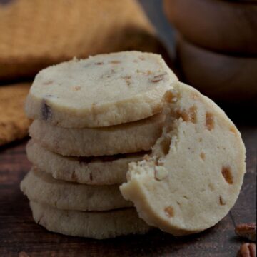 A stack of five cookies with another cookie leaning on the stack of cookies. It has a bite out of it.