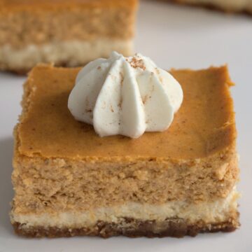 A pumpkin cheesecake bar on a white plate. More bars are in the background.