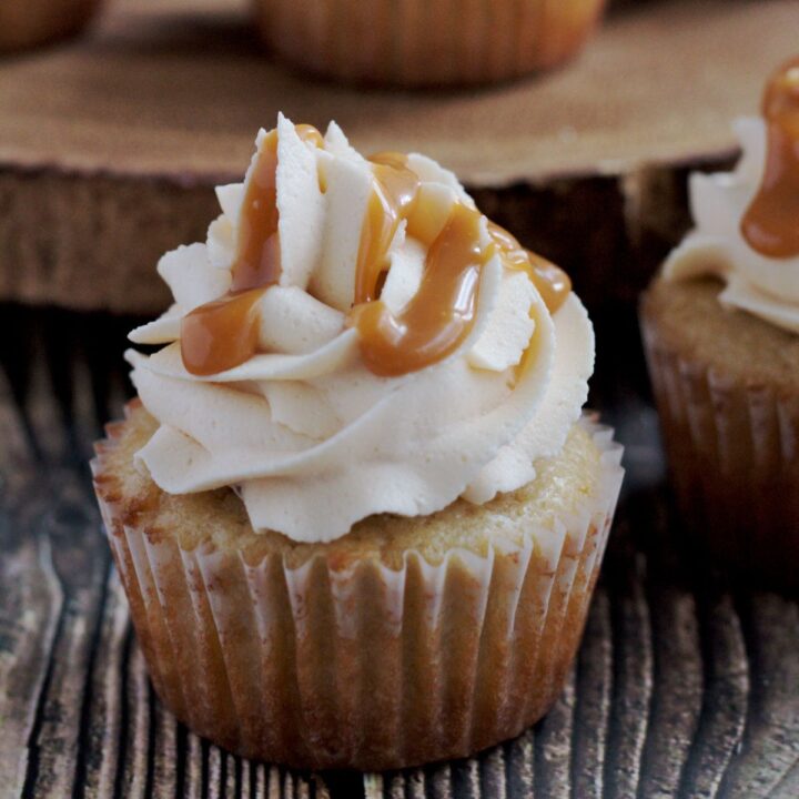 A single cupcake on a wooden surface. More cupcakes are in the background.