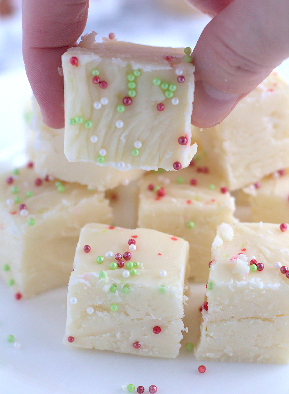 A bunch of fudge pieces on a white. plate. A pieces of fudge is lifted up.