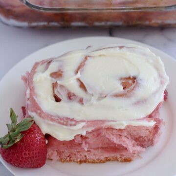 A cinnamon roll on a white plate. A strawberry sits next to it.