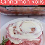 A cinnamon roll on a white plate. A strawberry sits next to it.