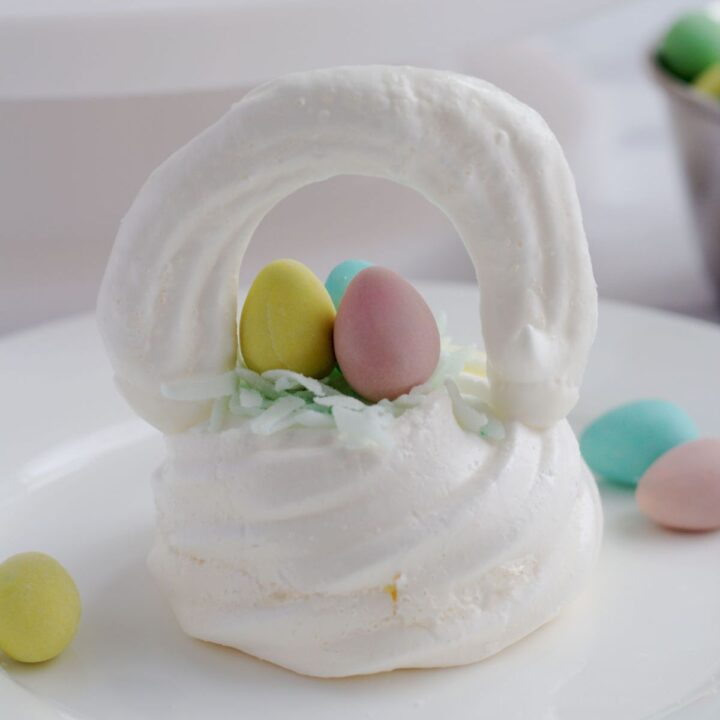 A meringue Easter basket on a white plate. Some mini eggs are around the basket.