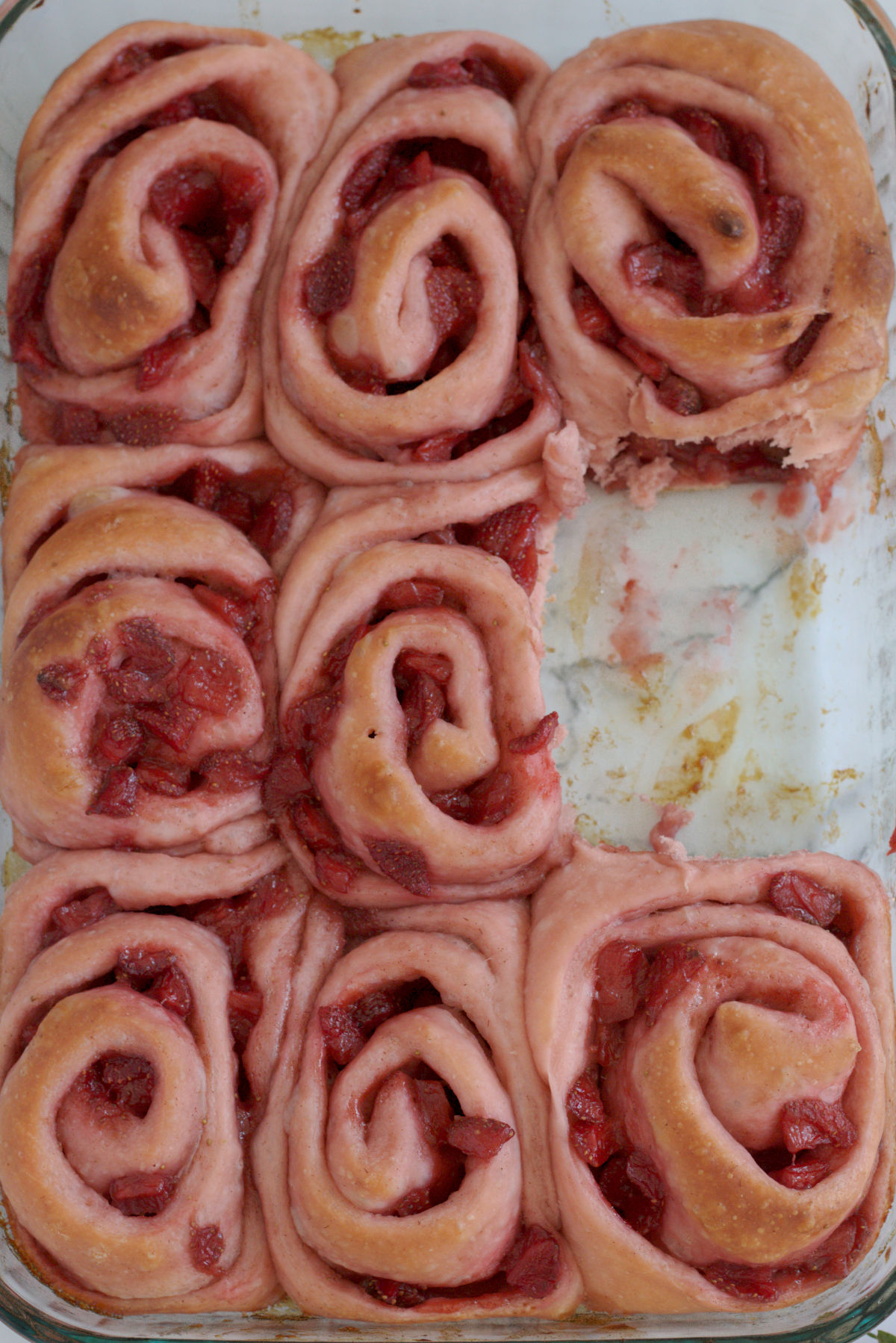 A baking dish with unfrosted cinnamon rolls in it. One cinnamon roll is missing.