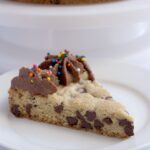A slice of cookie cake on a white plate.
