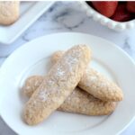 Ladyfinger cookies on a white plate. Some strawberries are in a white dish in the background.