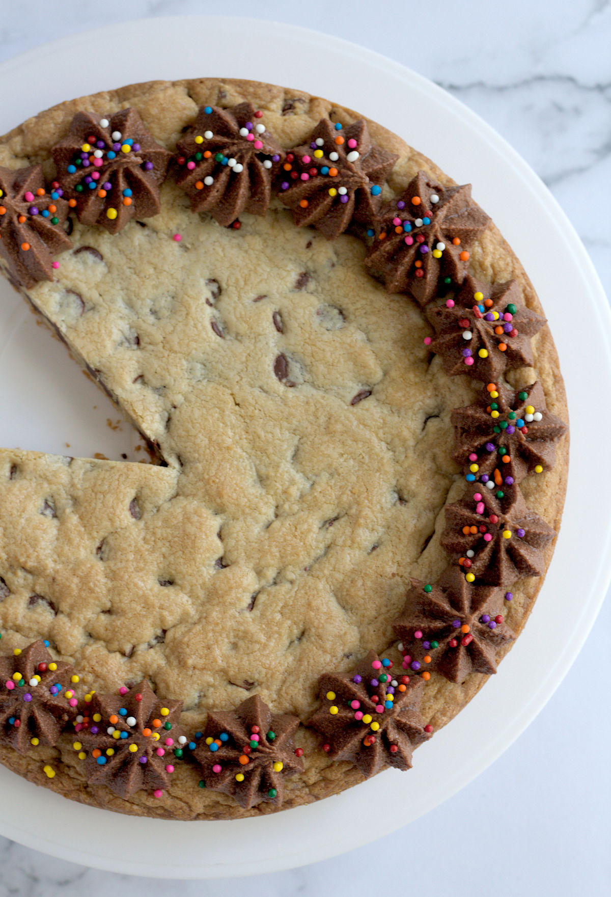 A top view of a cookie cake. A slice is missing from the cake.