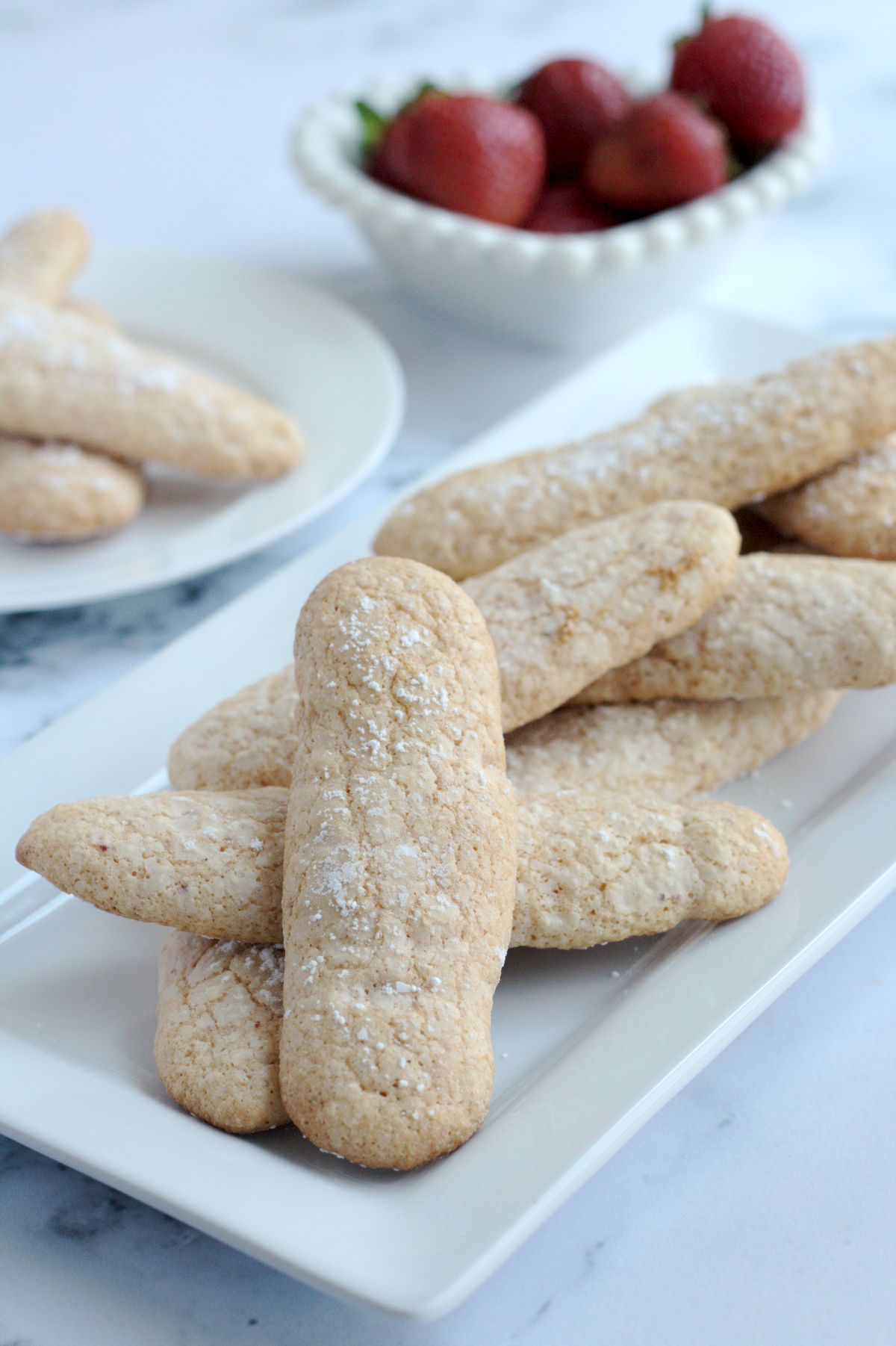 A bunch of ladyfinger cookies on a white platter.