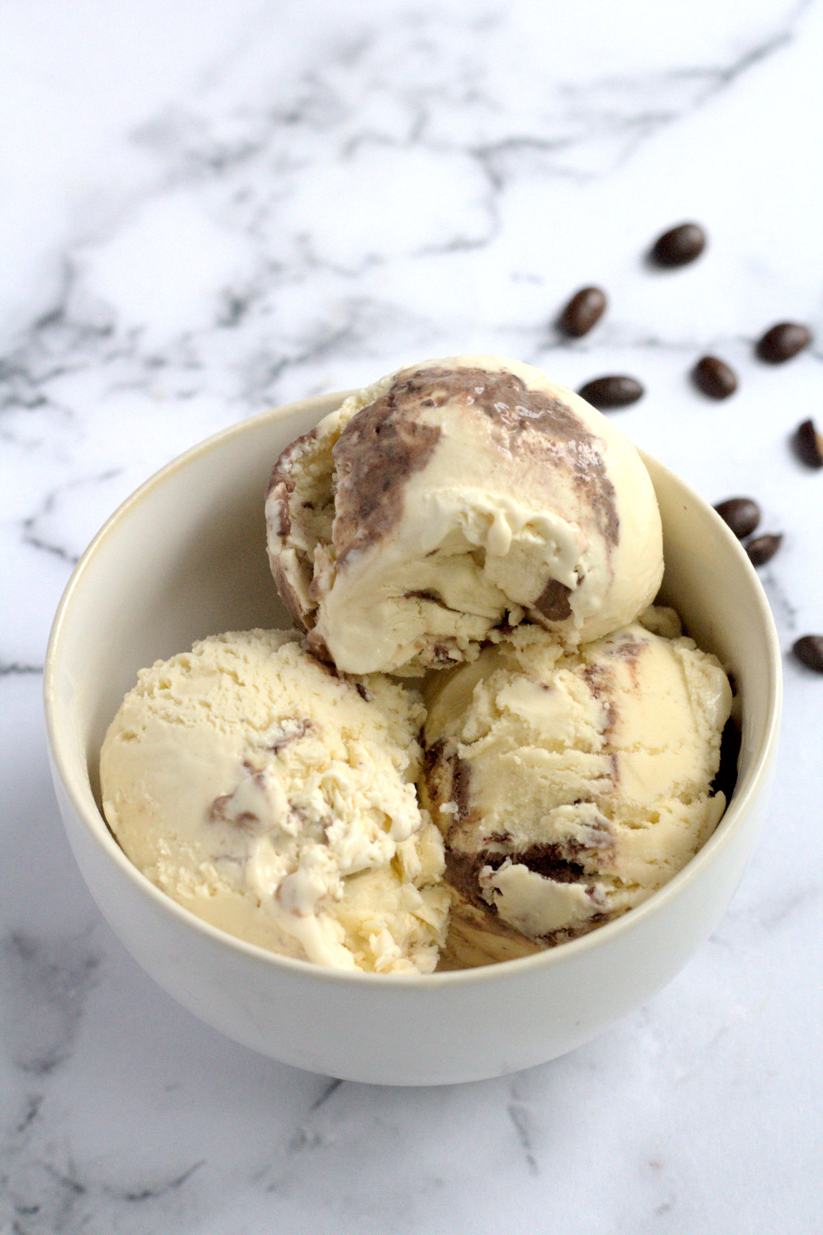 A white bowl with three scoops of ice cream in it. Coffee granules are around the bowl.