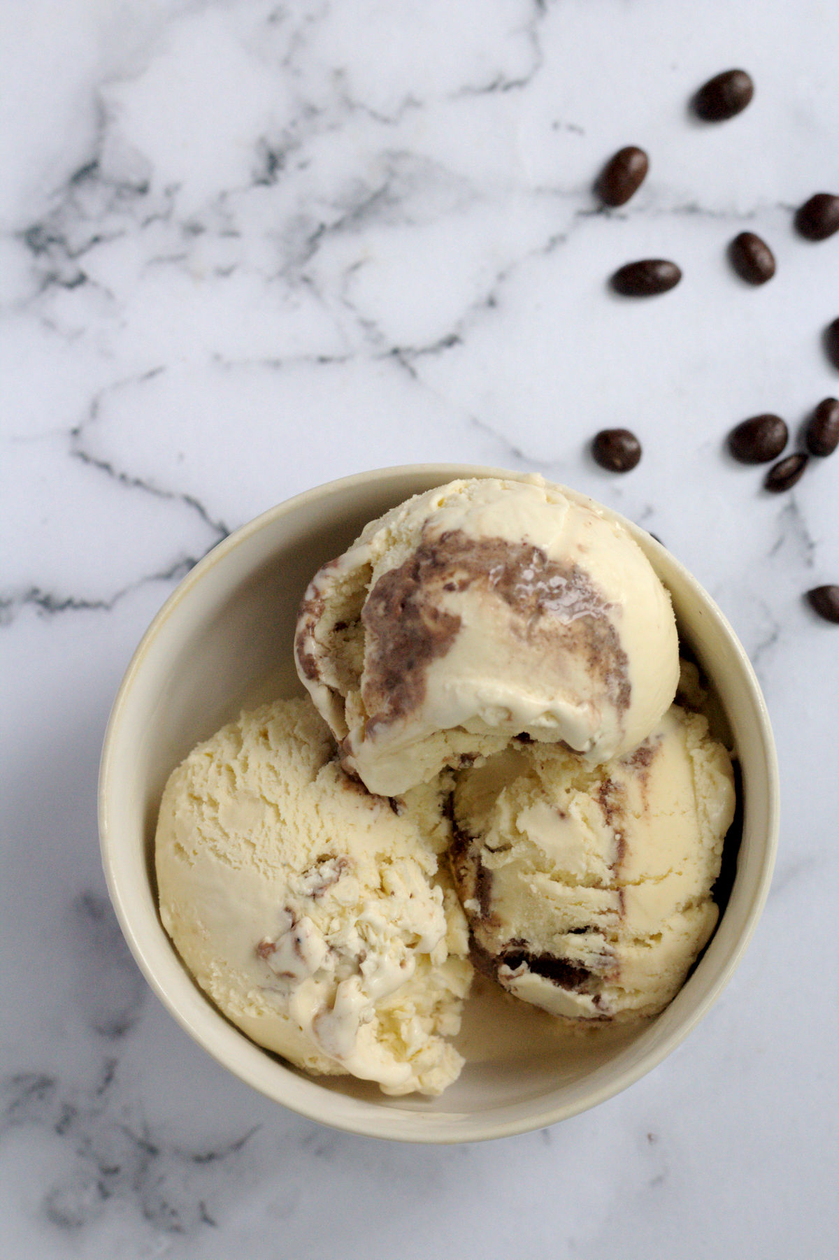 A white bowl with three scoops of ice cream in it. Coffee granules are around the bowl.