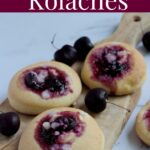 A bunch of kolaches on a wooden board with cherries around it.