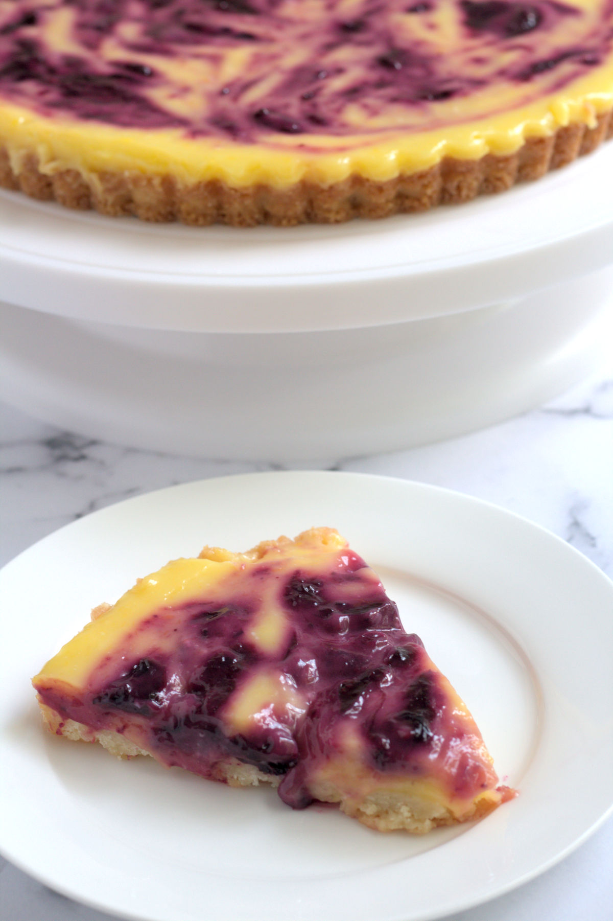A slice of tart on a white plate. The rest of the tart can be partially seen in the background.