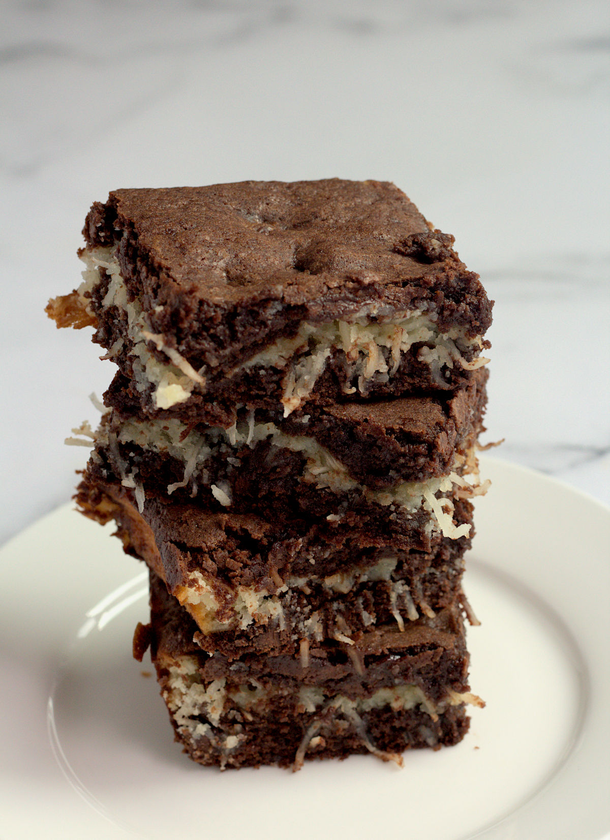 A stack of four brownies on a white plate.