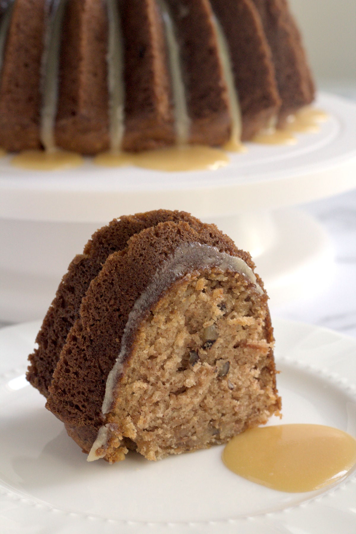 A slice of cake on a white plate. Some caramel is on the plate too.