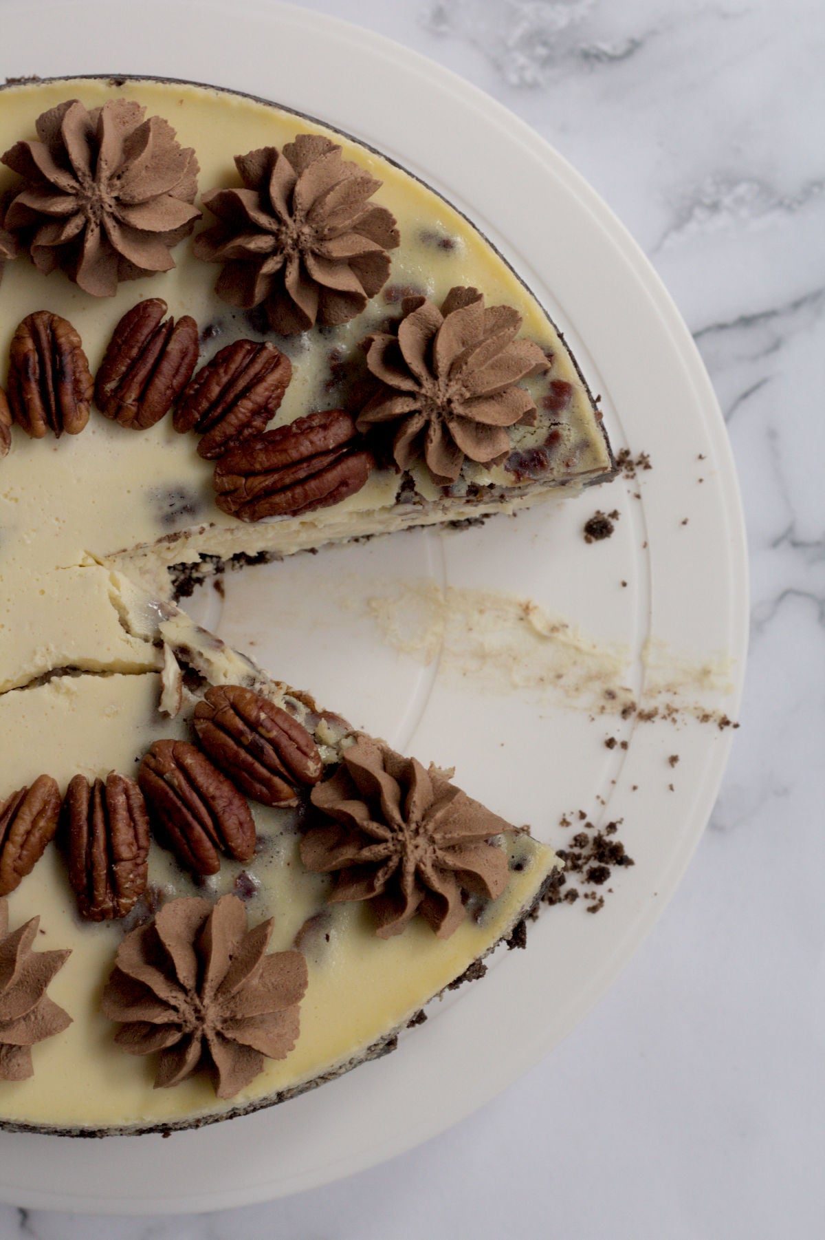 An above view of a cheesecake on a white cake plate. A piece of cheesecake is missing.